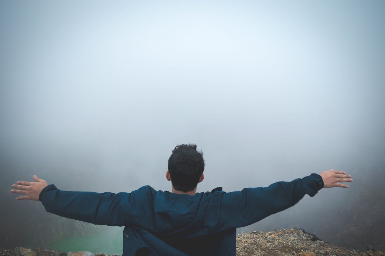 A man stands on a foggy cliff with arms outstretched, embracing freedom and nature.